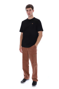 A man modeling a black crewneck t-shirt and brown corduroy cargo pants against a solid white background.