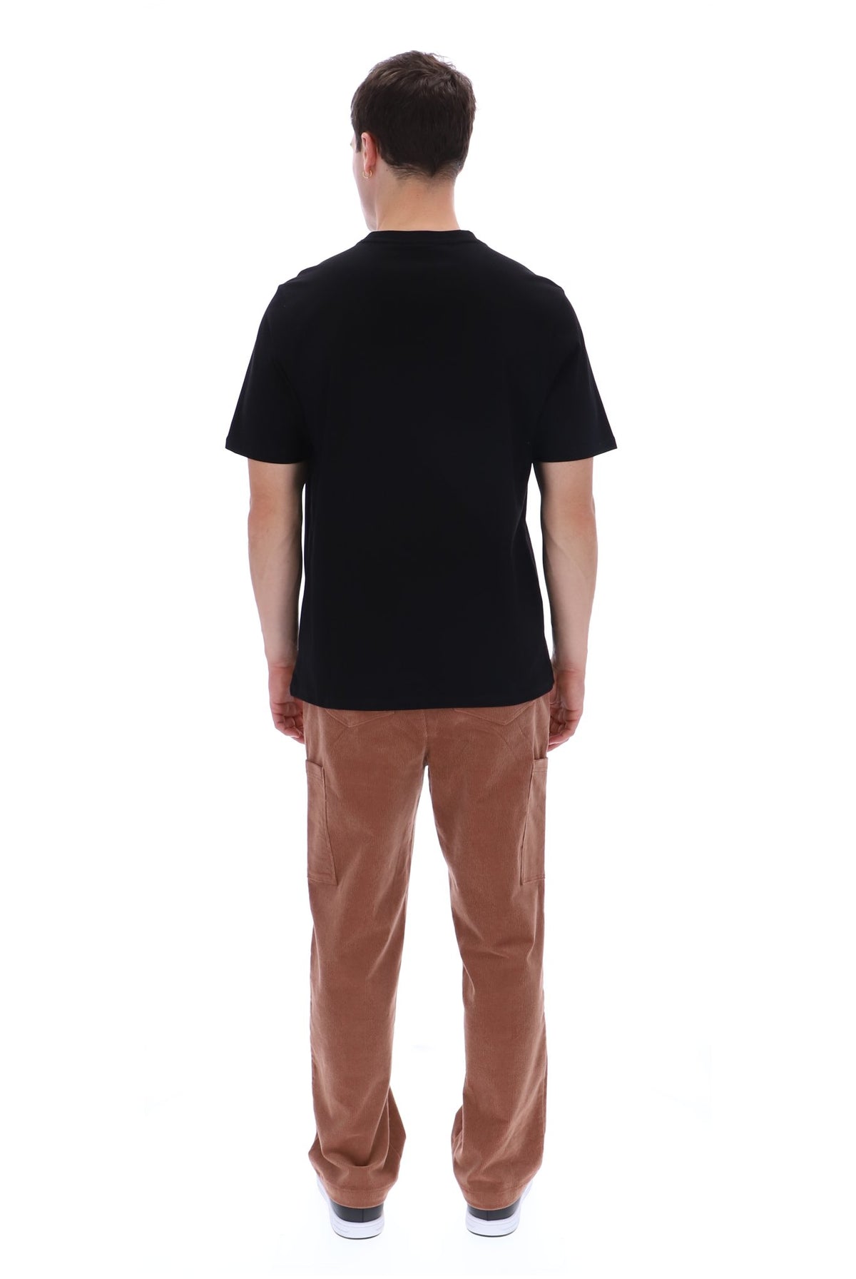 A man viewed from the back wearing a black short-sleeve t-shirt and brown corduroy pants against a plain white background.