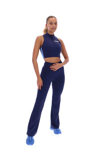 A woman wearing a navy blue zip-up crop top with seamless look and FILA x TALA logo branded on the front.