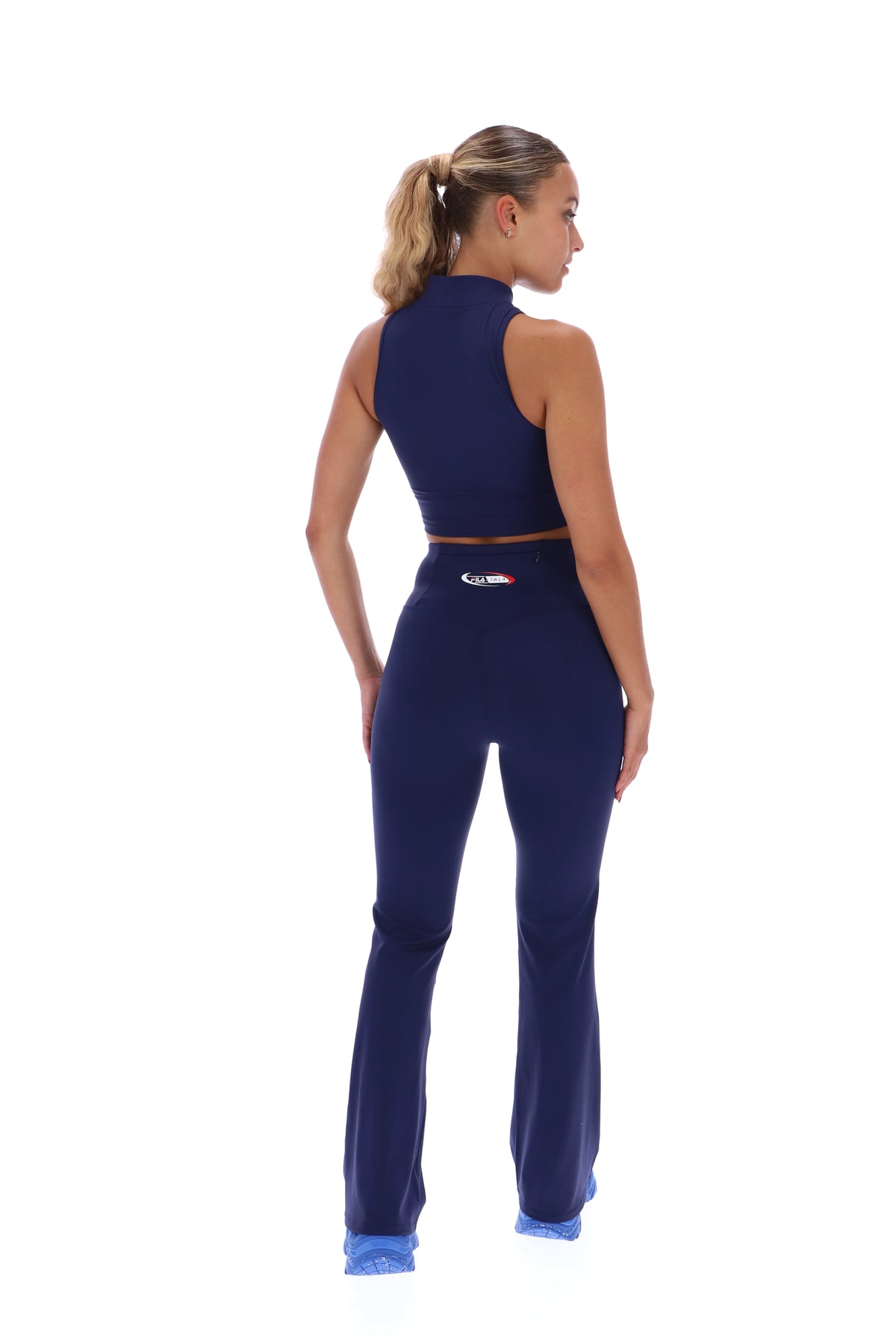 A woman wearing a navy blue zip-up crop top, paired with matching leggings that feature a FILA x TALA logo branded on the back.