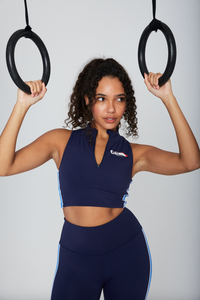 A woman wearing a navy blue zip-up crop top with seamless look and FILA x TALA logo branded on the front.